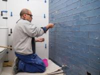 Senior murer arbejder på knæ på badeværelsesvæg
