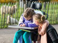 Socialpædagog står ved et barn i kørestol